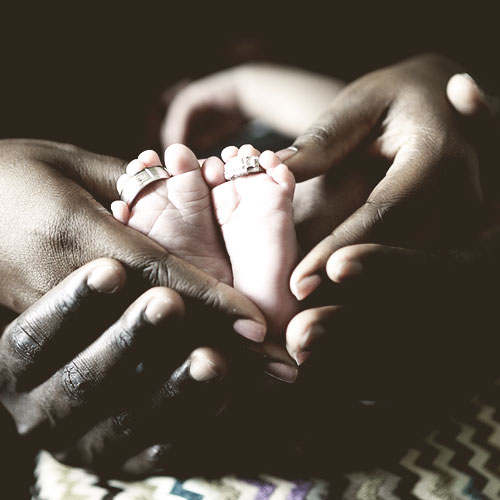 Image of a couple holding their babies feet with their marriage rings on the toes