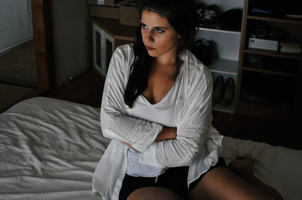 Image of a girl sitting on her bed upset with her arms crossed